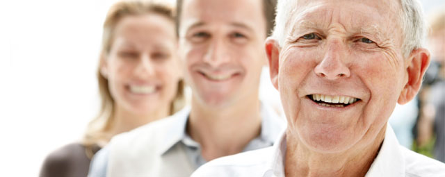 An older gentleman, a young man and a woman stood in a line smiling