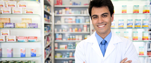A male pharmacist stood with his arms crossed in front of medication shelves